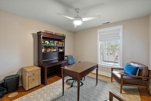 office area with a ceiling fan, visible vents, baseboards, and wood finished floors