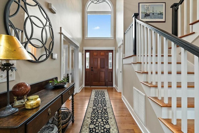 foyer entrance with a high ceiling, light wood finished floors, stairway, and visible vents