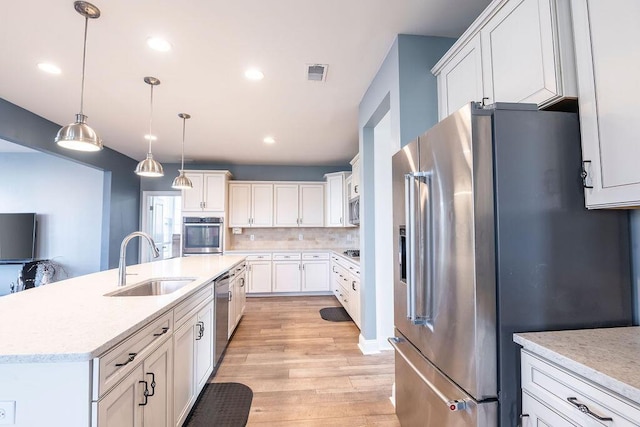 kitchen with appliances with stainless steel finishes, a center island with sink, white cabinets, decorative light fixtures, and sink