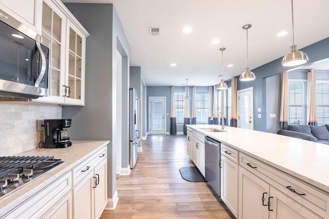 kitchen with light wood-type flooring, stainless steel appliances, decorative backsplash, pendant lighting, and sink