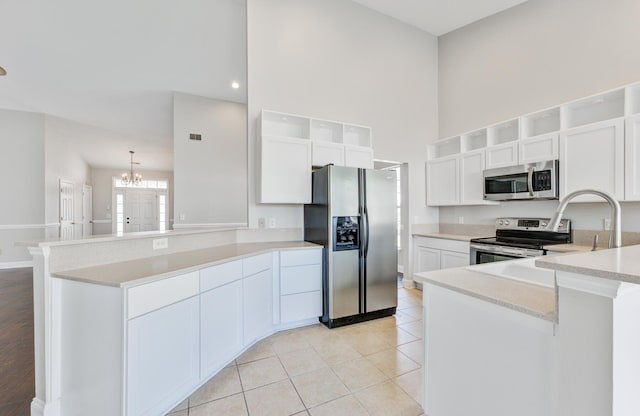 kitchen featuring kitchen peninsula, white cabinets, light tile patterned floors, an inviting chandelier, and stainless steel appliances