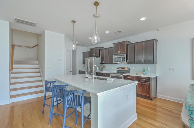 kitchen featuring a kitchen bar, sink, a center island with sink, pendant lighting, and stainless steel appliances