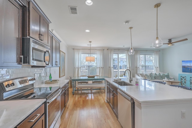 kitchen featuring decorative light fixtures, sink, dark brown cabinetry, stainless steel appliances, and a center island with sink