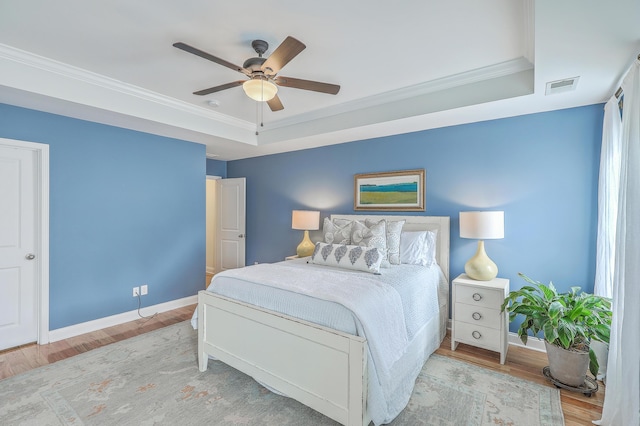 bedroom with hardwood / wood-style floors, crown molding, and a raised ceiling