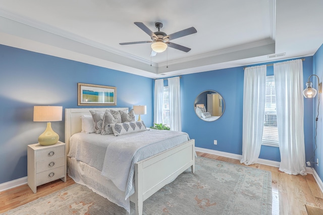 bedroom with multiple windows, a tray ceiling, and light hardwood / wood-style flooring