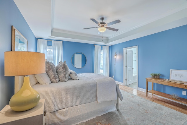 bedroom with crown molding, ceiling fan, connected bathroom, a raised ceiling, and light wood-type flooring