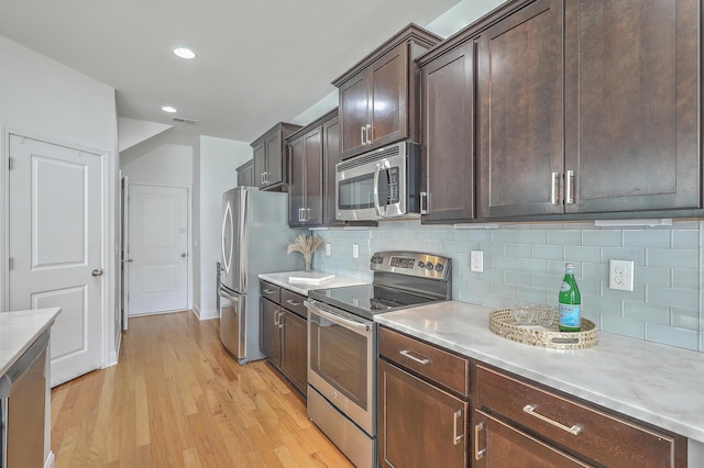 kitchen with decorative backsplash, stainless steel appliances, dark brown cabinets, and light wood-type flooring