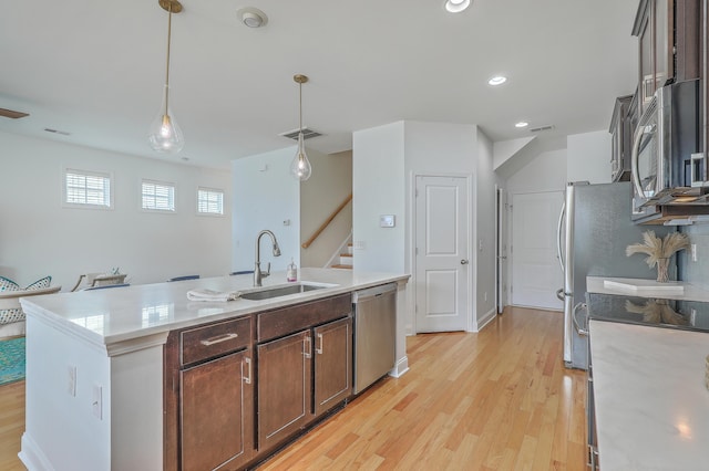 kitchen featuring dark brown cabinetry, sink, decorative light fixtures, stainless steel appliances, and a kitchen island with sink