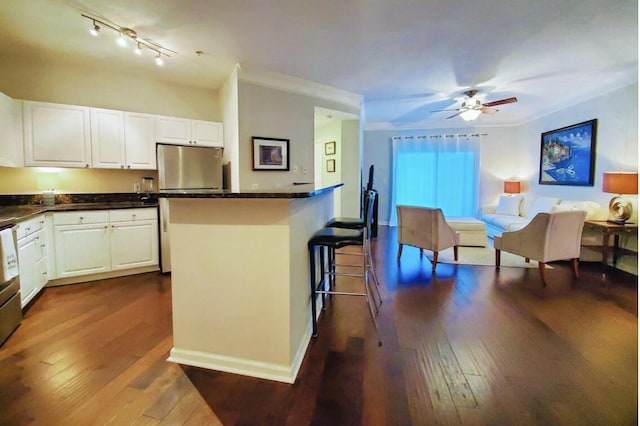 kitchen featuring white cabinets, dark hardwood / wood-style floors, fridge, crown molding, and a breakfast bar area