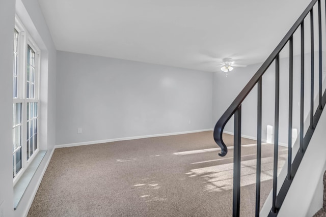 empty room with carpet floors, a ceiling fan, baseboards, and stairs