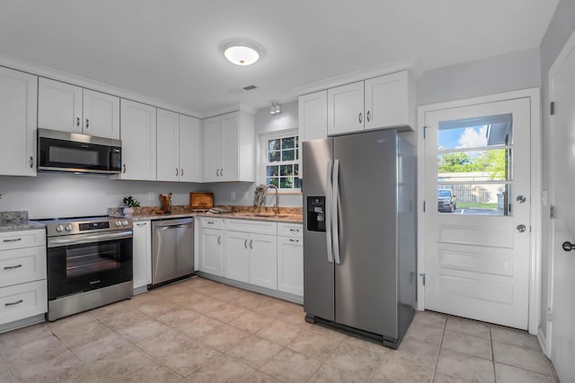 kitchen with appliances with stainless steel finishes, a sink, light stone counters, white cabinets, and light tile patterned floors
