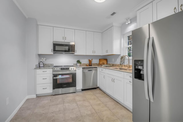 kitchen with appliances with stainless steel finishes, a sink, white cabinets, and light stone countertops