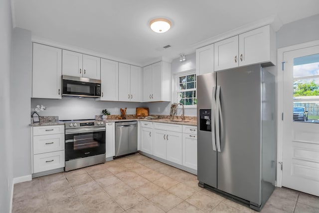 kitchen with appliances with stainless steel finishes, light stone counters, white cabinets, a sink, and light tile patterned floors
