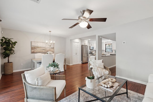 living area featuring a ceiling fan, a chandelier, baseboards, and dark wood-style flooring