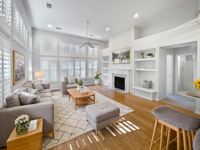 living room with built in shelves, ceiling fan, and light hardwood / wood-style floors