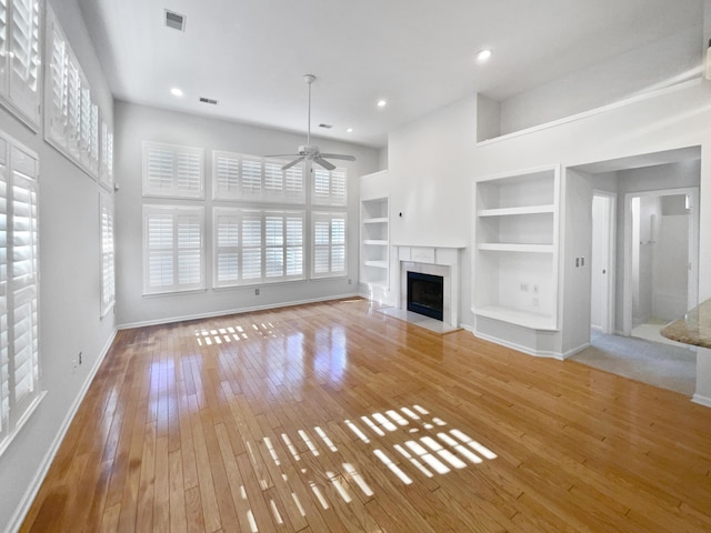 unfurnished living room with built in shelves, ceiling fan, and light hardwood / wood-style floors