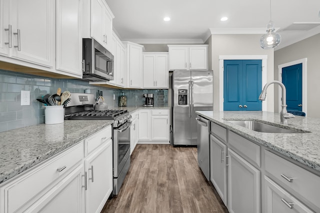 kitchen with hanging light fixtures, appliances with stainless steel finishes, white cabinetry, hardwood / wood-style flooring, and sink