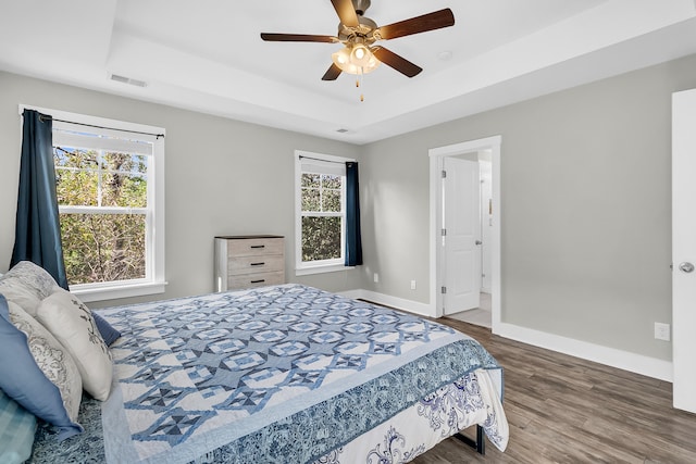 bedroom featuring a raised ceiling, hardwood / wood-style flooring, multiple windows, and ceiling fan