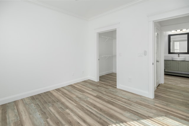 unfurnished bedroom with a walk in closet, light hardwood / wood-style floors, sink, ensuite bathroom, and crown molding