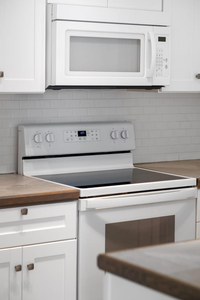 kitchen featuring white cabinets, backsplash, wood counters, and white appliances