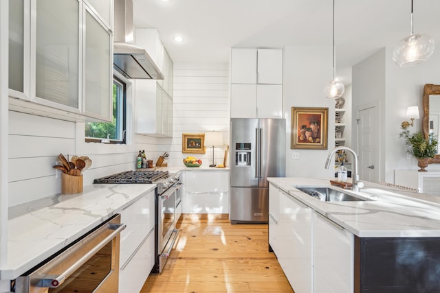 kitchen with sink, high quality appliances, an island with sink, white cabinets, and exhaust hood