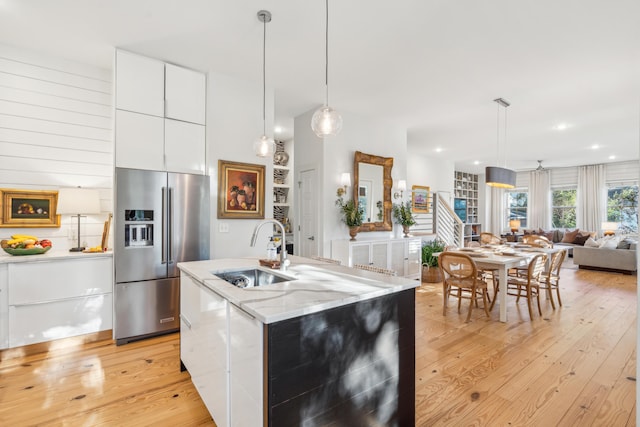 kitchen featuring sink, light stone countertops, white cabinets, a center island with sink, and high end refrigerator