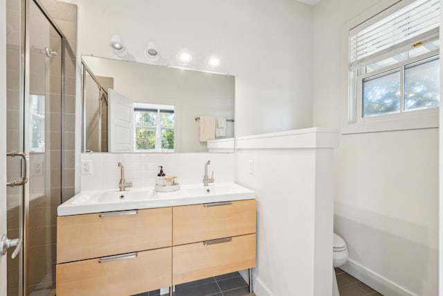 bathroom featuring toilet, vanity, a shower with door, tile patterned flooring, and decorative backsplash