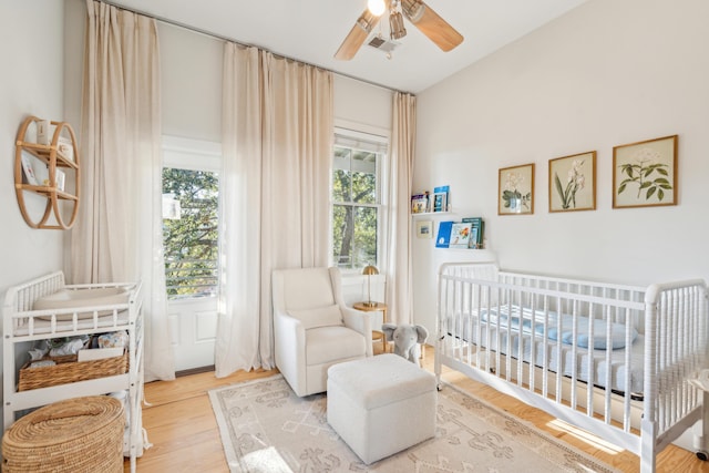 bedroom featuring a crib, wood-type flooring, and ceiling fan