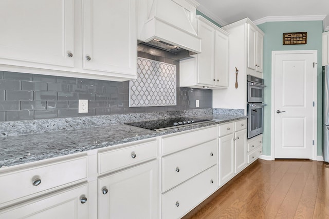 kitchen featuring custom range hood, white cabinetry, double oven, crown molding, and black electric stovetop