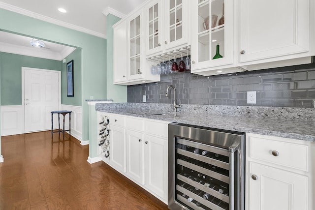 kitchen featuring beverage cooler, a wainscoted wall, ornamental molding, light stone counters, and dark wood-style flooring