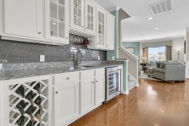 kitchen with visible vents, backsplash, beverage cooler, white cabinetry, and a sink