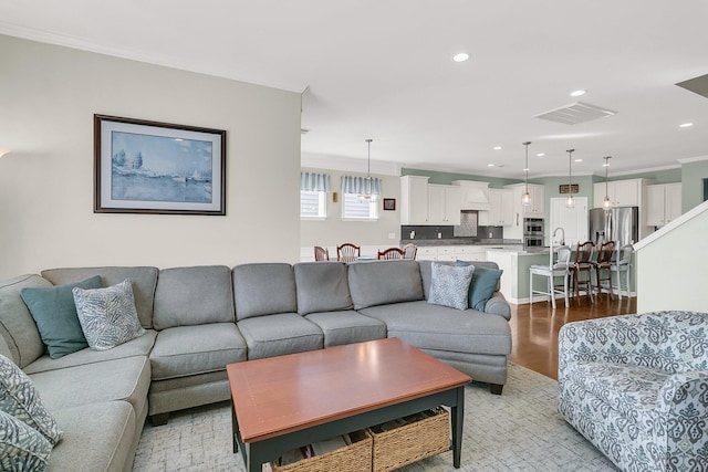 living area with recessed lighting, visible vents, ornamental molding, and light wood finished floors