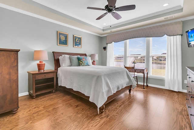 bedroom featuring a tray ceiling, baseboards, visible vents, and wood finished floors