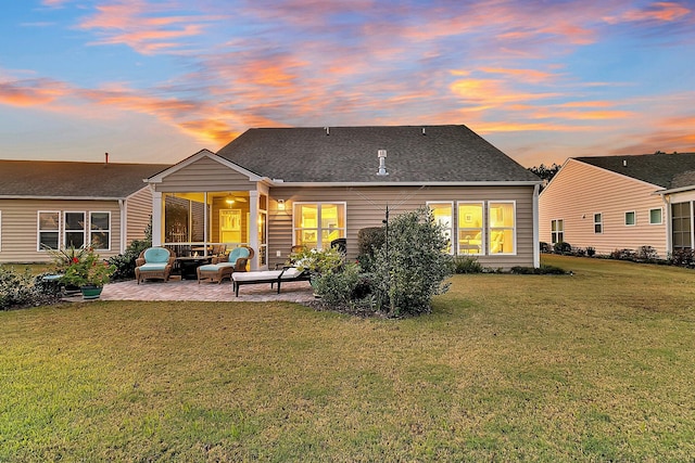 back of property at dusk featuring a yard, roof with shingles, and a patio area