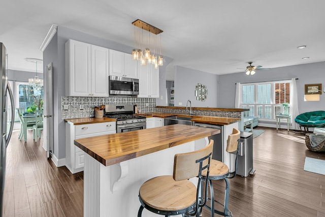 kitchen featuring kitchen peninsula, pendant lighting, wooden counters, sink, and stainless steel appliances