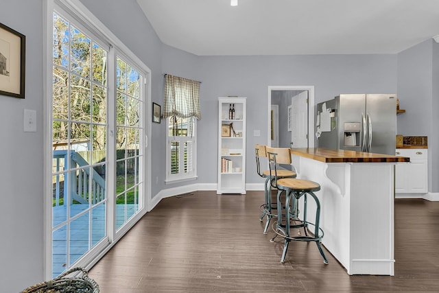 kitchen with dark wood-type flooring, white cabinetry, stainless steel fridge with ice dispenser, butcher block countertops, and a breakfast bar area