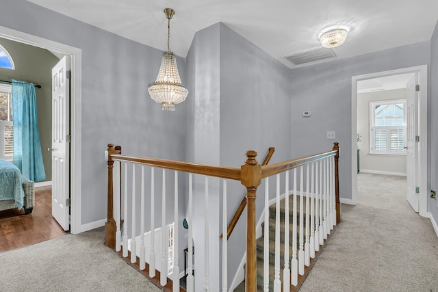 corridor with light carpet and a notable chandelier