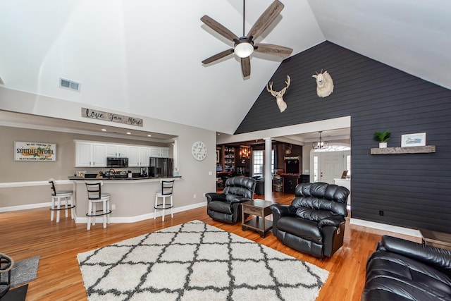 living room featuring decorative columns, visible vents, a ceiling fan, light wood-type flooring, and high vaulted ceiling