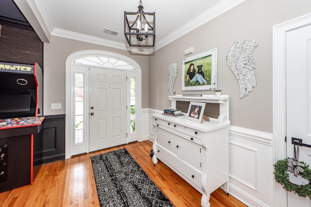 entryway with a notable chandelier, visible vents, wainscoting, light wood-type flooring, and crown molding