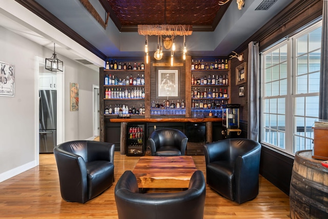 bar featuring freestanding refrigerator, a raised ceiling, a bar, and wood finished floors