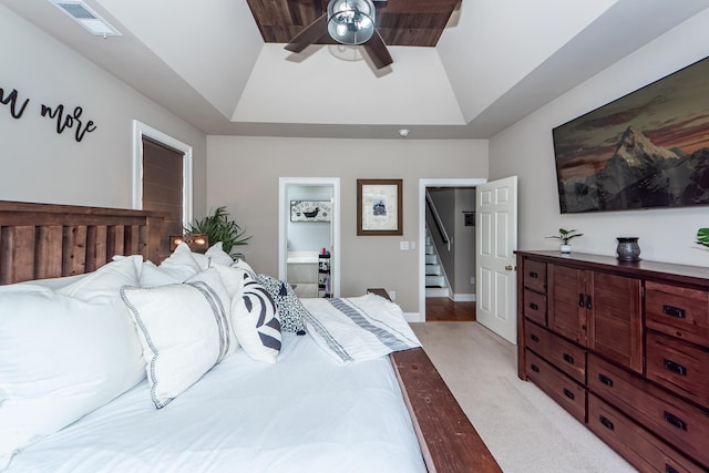 bedroom featuring ceiling fan, ensuite bathroom, light colored carpet, visible vents, and a tray ceiling