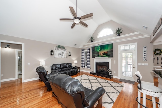 living area with a fireplace with raised hearth, high vaulted ceiling, light wood finished floors, and baseboards