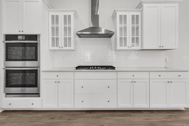 kitchen with decorative backsplash, appliances with stainless steel finishes, dark hardwood / wood-style flooring, wall chimney range hood, and white cabinetry