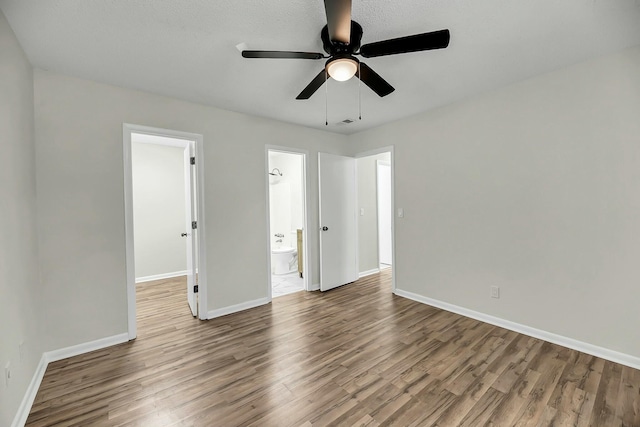 unfurnished bedroom featuring ensuite bath, baseboards, ceiling fan, and wood finished floors