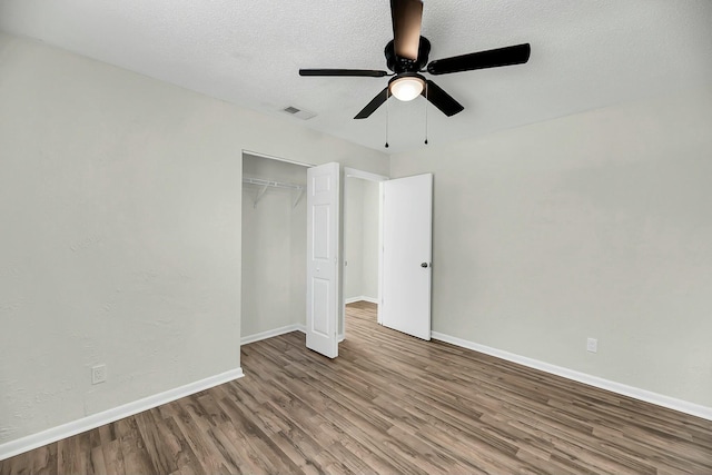 unfurnished bedroom with a closet, a textured ceiling, baseboards, and wood finished floors