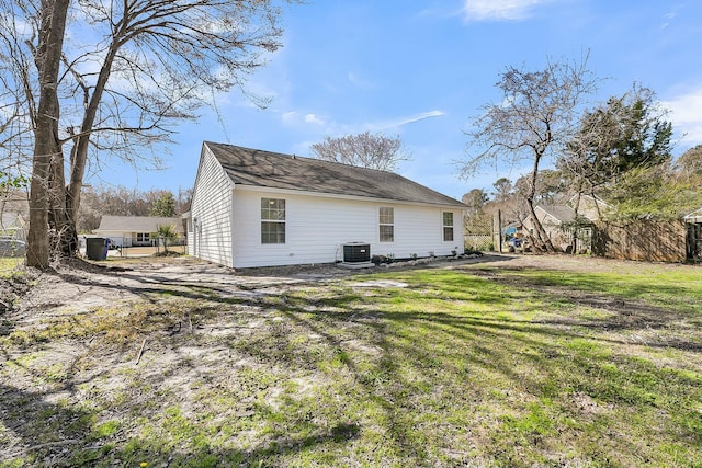 rear view of house featuring central AC unit, a lawn, and fence