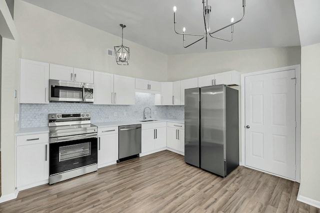 kitchen with white cabinets, appliances with stainless steel finishes, hanging light fixtures, light countertops, and a sink