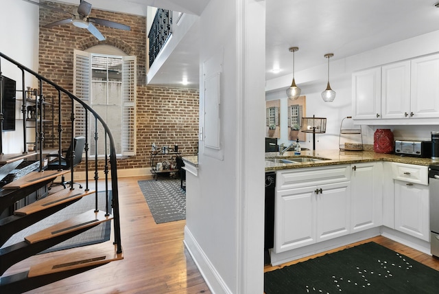 kitchen with brick wall, white cabinets, light wood-type flooring, dark stone counters, and decorative light fixtures