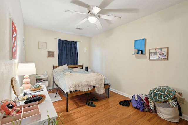 bedroom with a ceiling fan, visible vents, baseboards, and wood finished floors