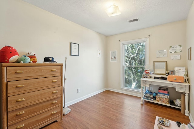 office with visible vents, a textured ceiling, baseboards, and wood finished floors